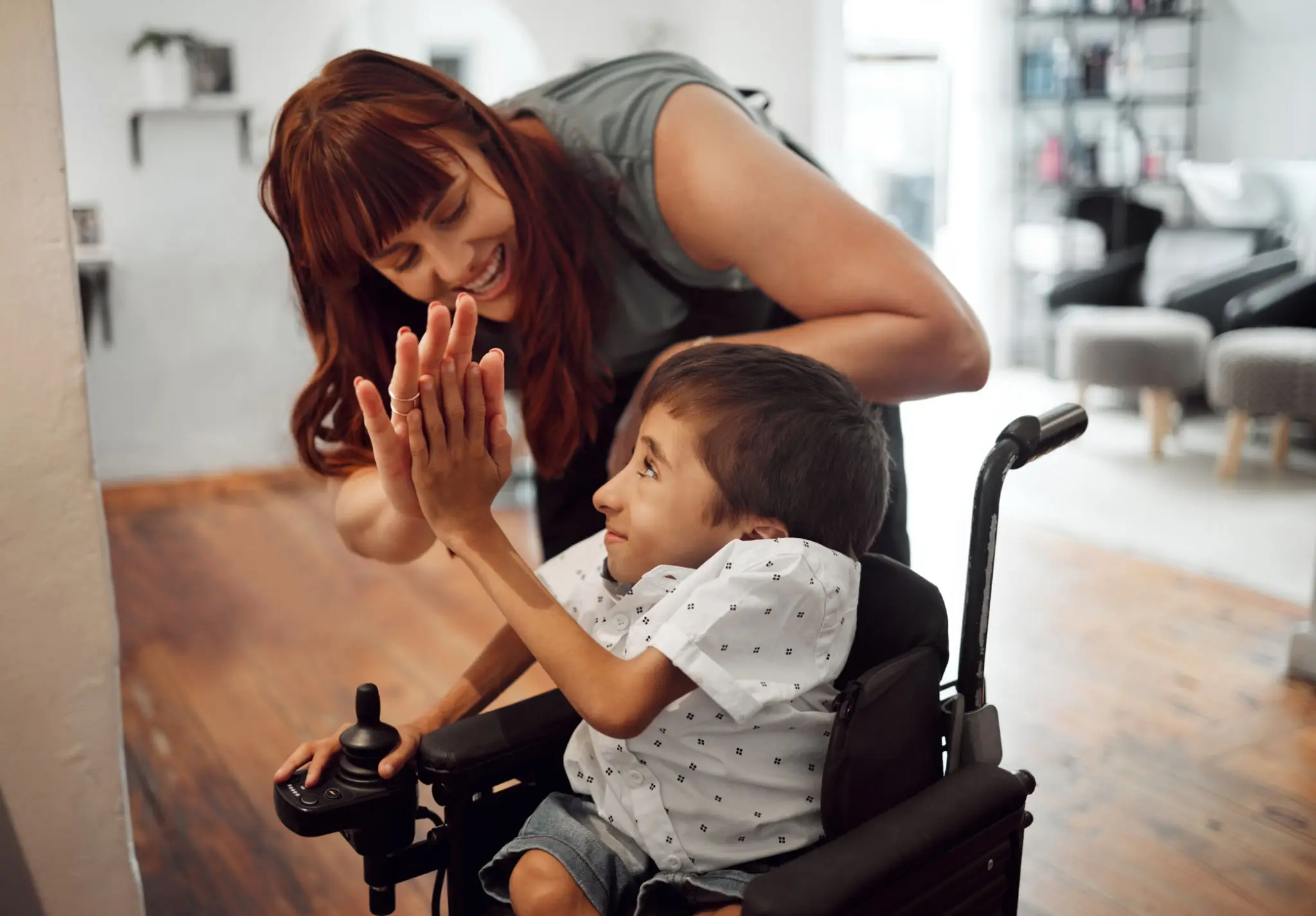 A woman joyfully high-fives a smiling child in a wheelchair.