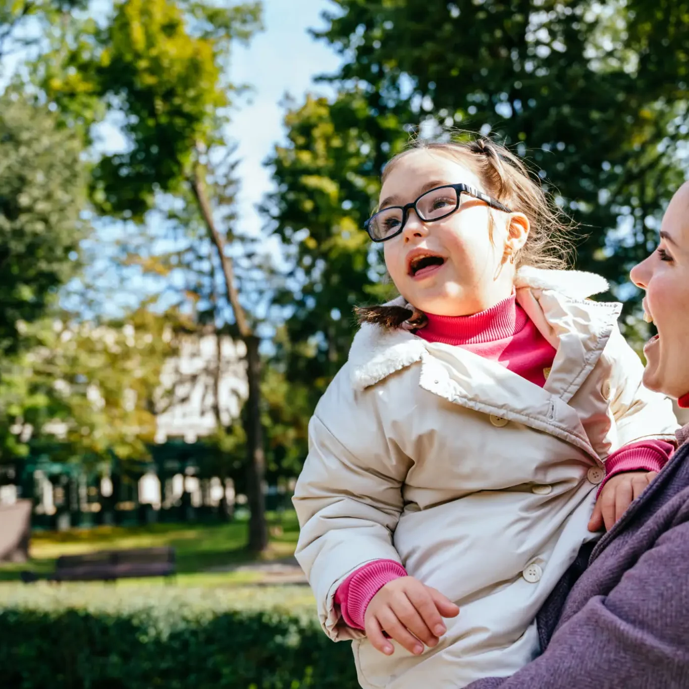 A joyful child being held by an adult in a sunlit park.